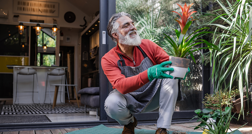 Smiling man gardening outside holding up a plant