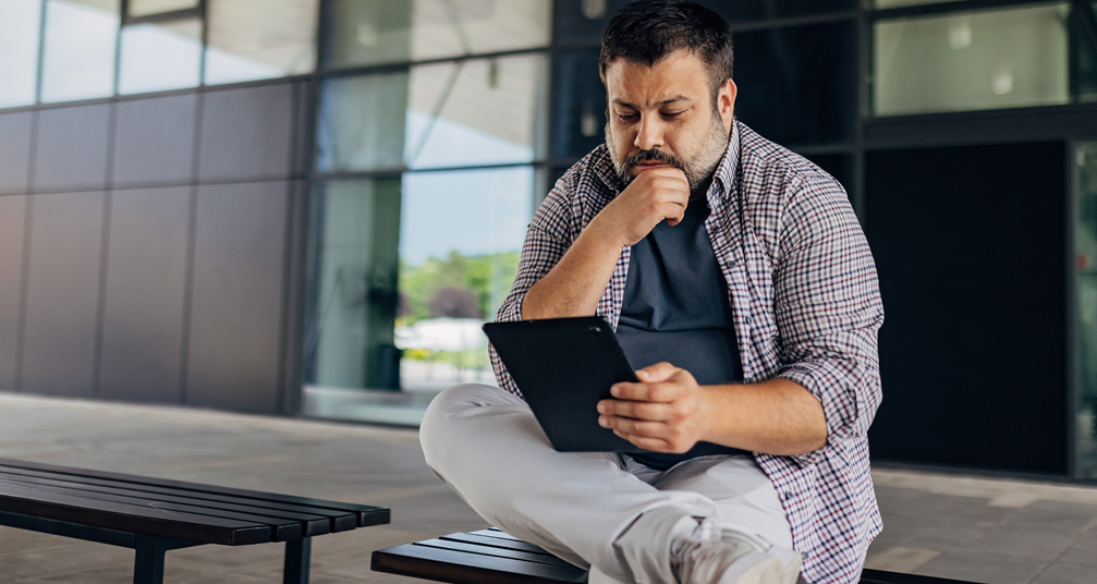 Man sitting on a bench reading from a tablet