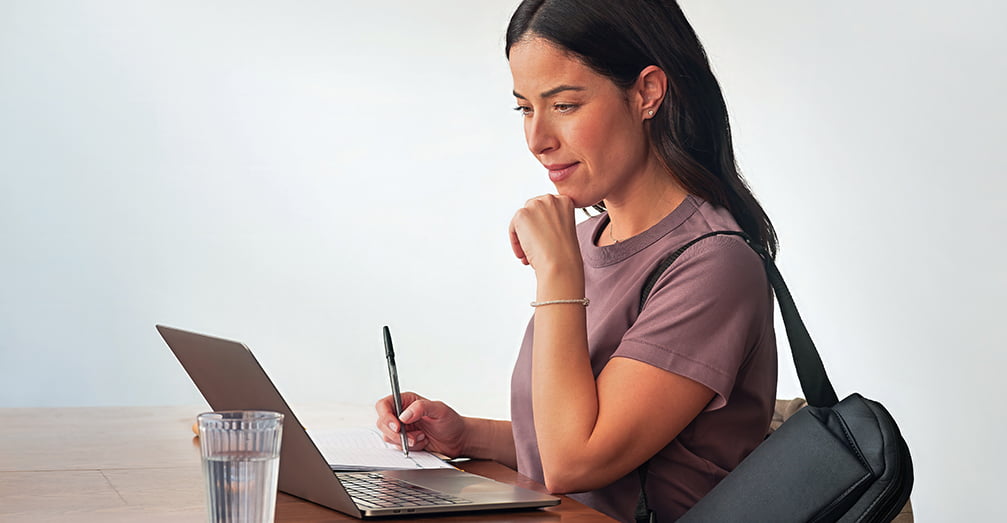 Woman taking notes while reading from a laptop