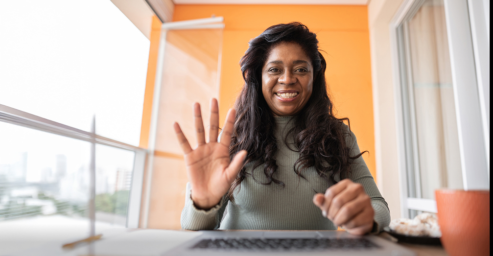 Smiling woman waving in front of a laptop